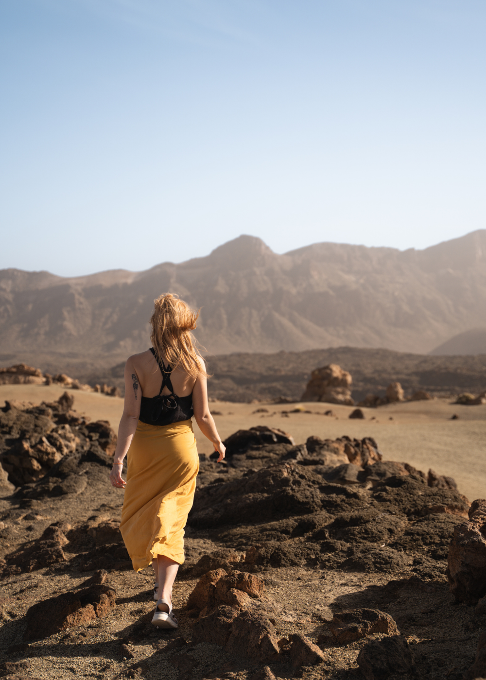 Female traveller heading in front on dessert in yellow skirt. Circular travel capsule wardrobe with sustainable and interchangeable clothing for travelling light, created for a minimal wardrobe and travelling in a carry-on only to avoid packing headache.