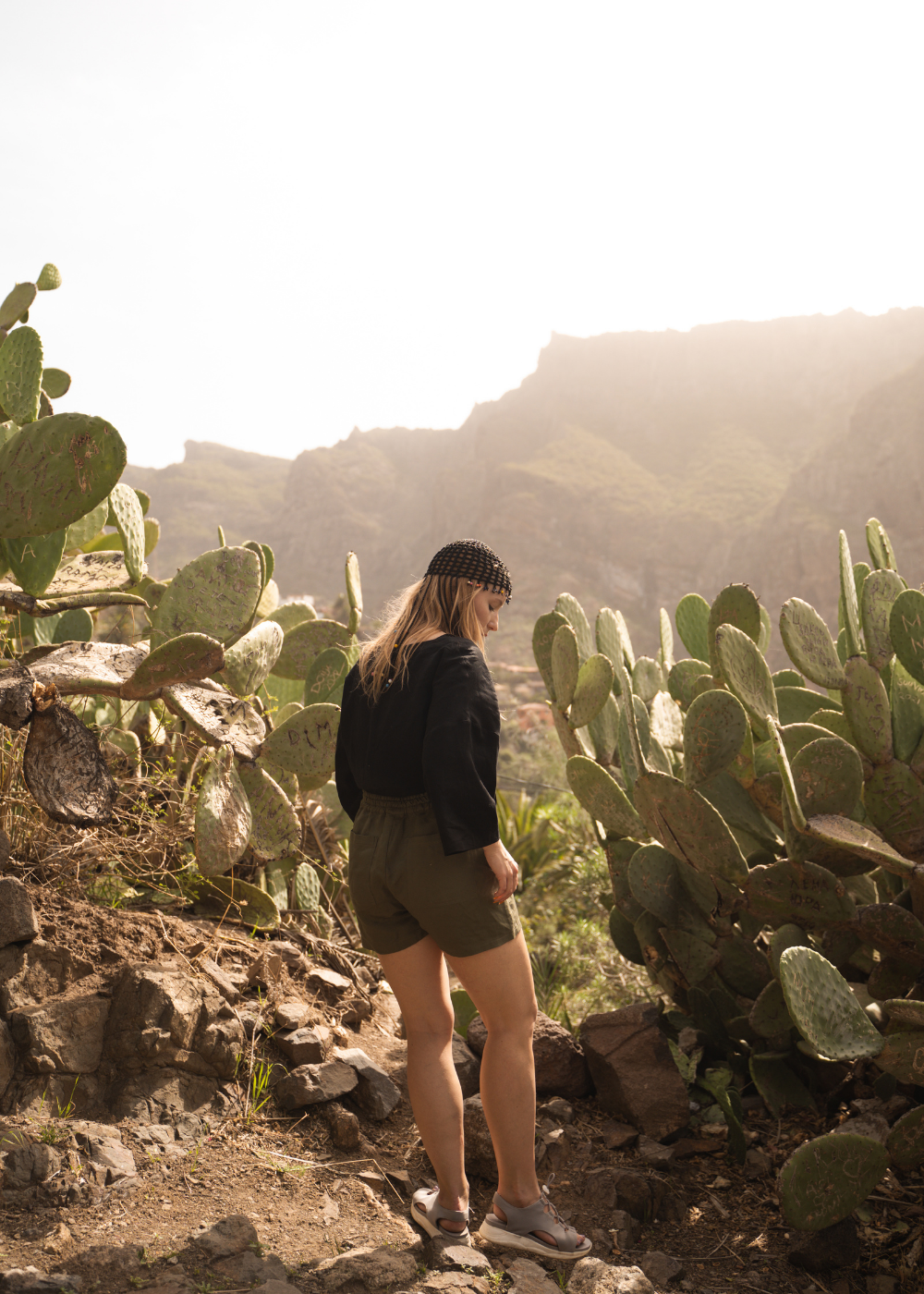 Female traveller standing among succulents. Circular travel capsule wardrobe with sustainable and interchangeable clothing for travelling light, created for a minimal wardrobe and travelling in a carry-on only to avoid packing headache.